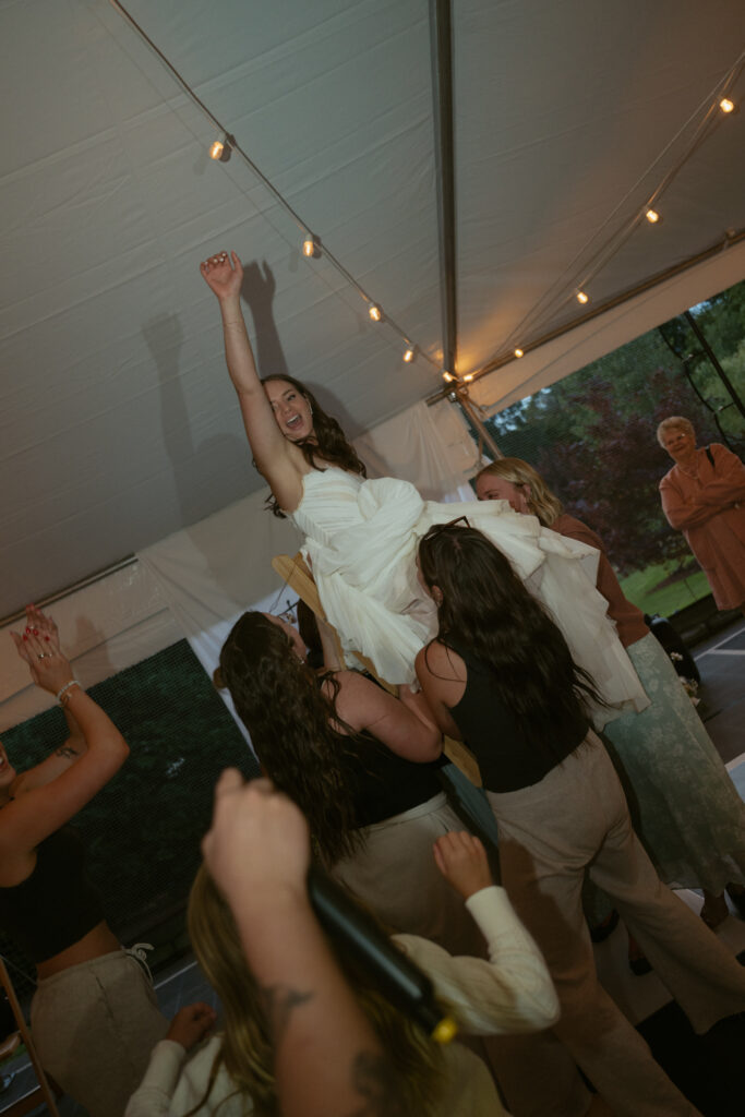 bride being lifted up dancing with guests under the tent 