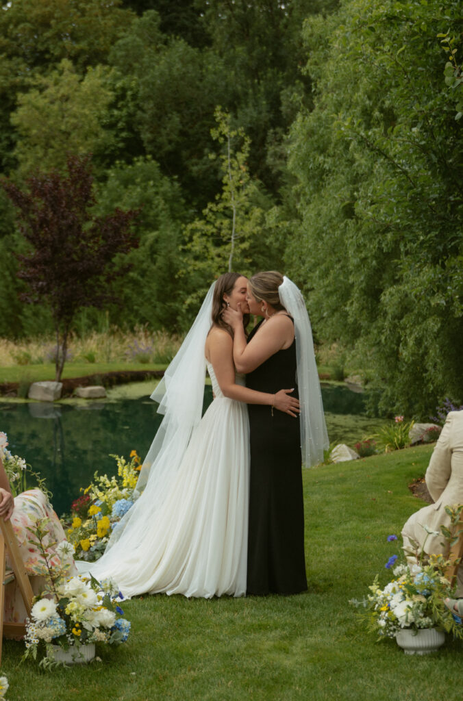 Alt text: Couple sharing their first kiss during an Oregon backyard wedding ceremony by the pond.